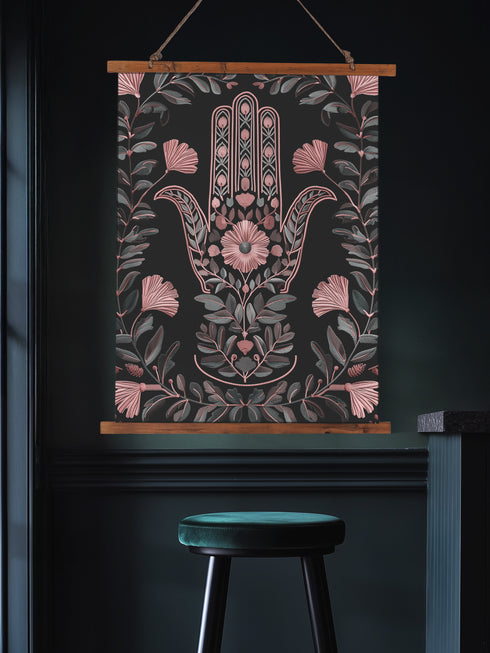 Botanical Hamsa wall tapestry featuring intricate rose gold and teal design on black background, showing a protective hand symbol surrounded by leaf motifs and floral elements, hanging from wooden dowels with natural twine.